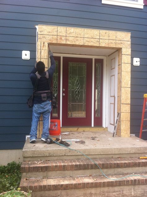 Contractor installing trim around an entry door on navy lap siding, North Jersey