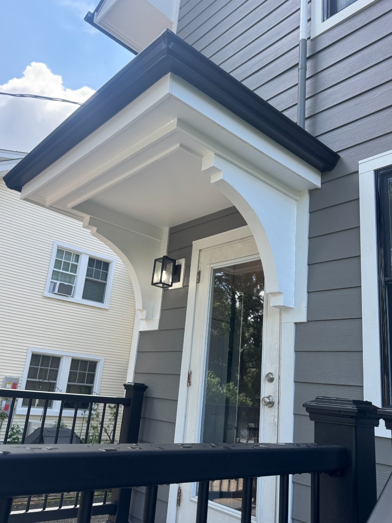 Trim surround at a front entry door on gray lap siding, North Jersey